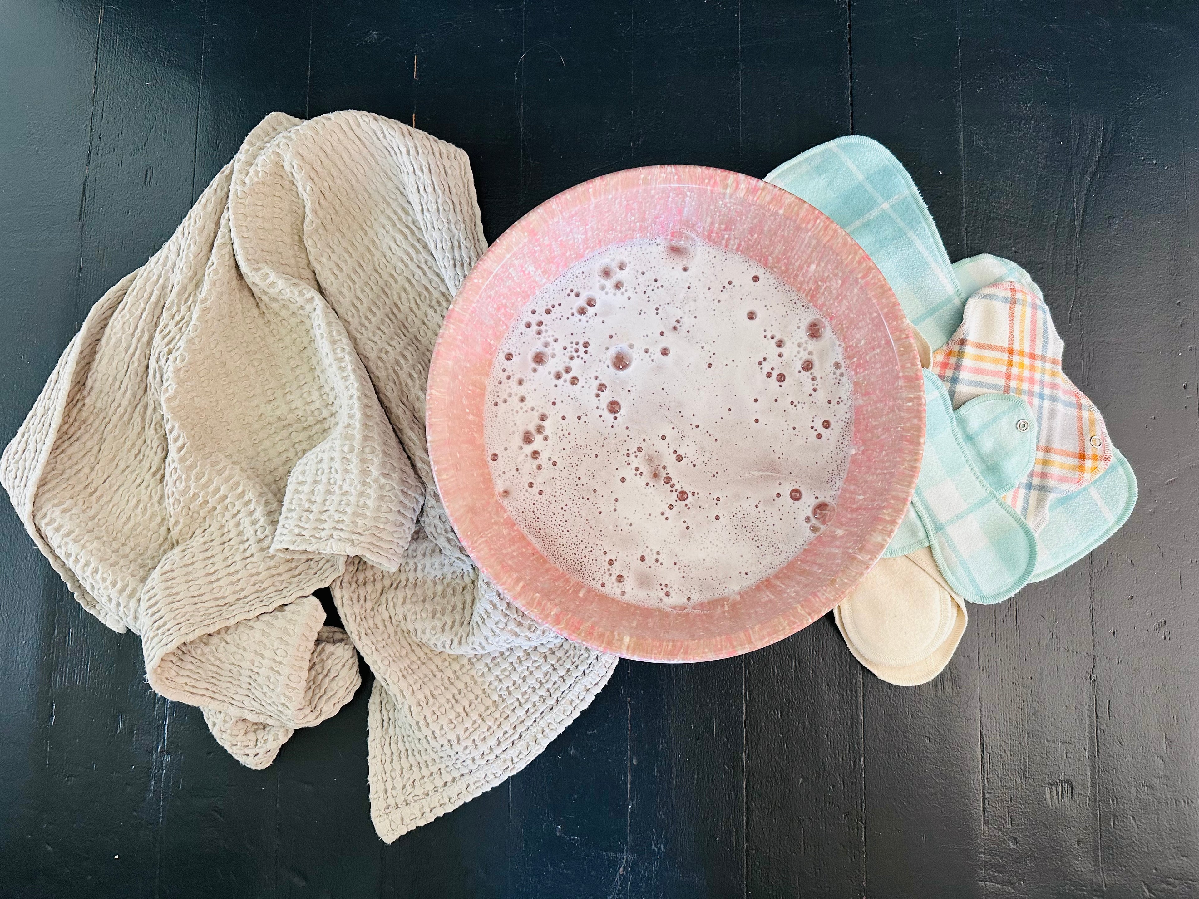 Bowl of soapy water with washcloth and gladrags reusable pads next to it