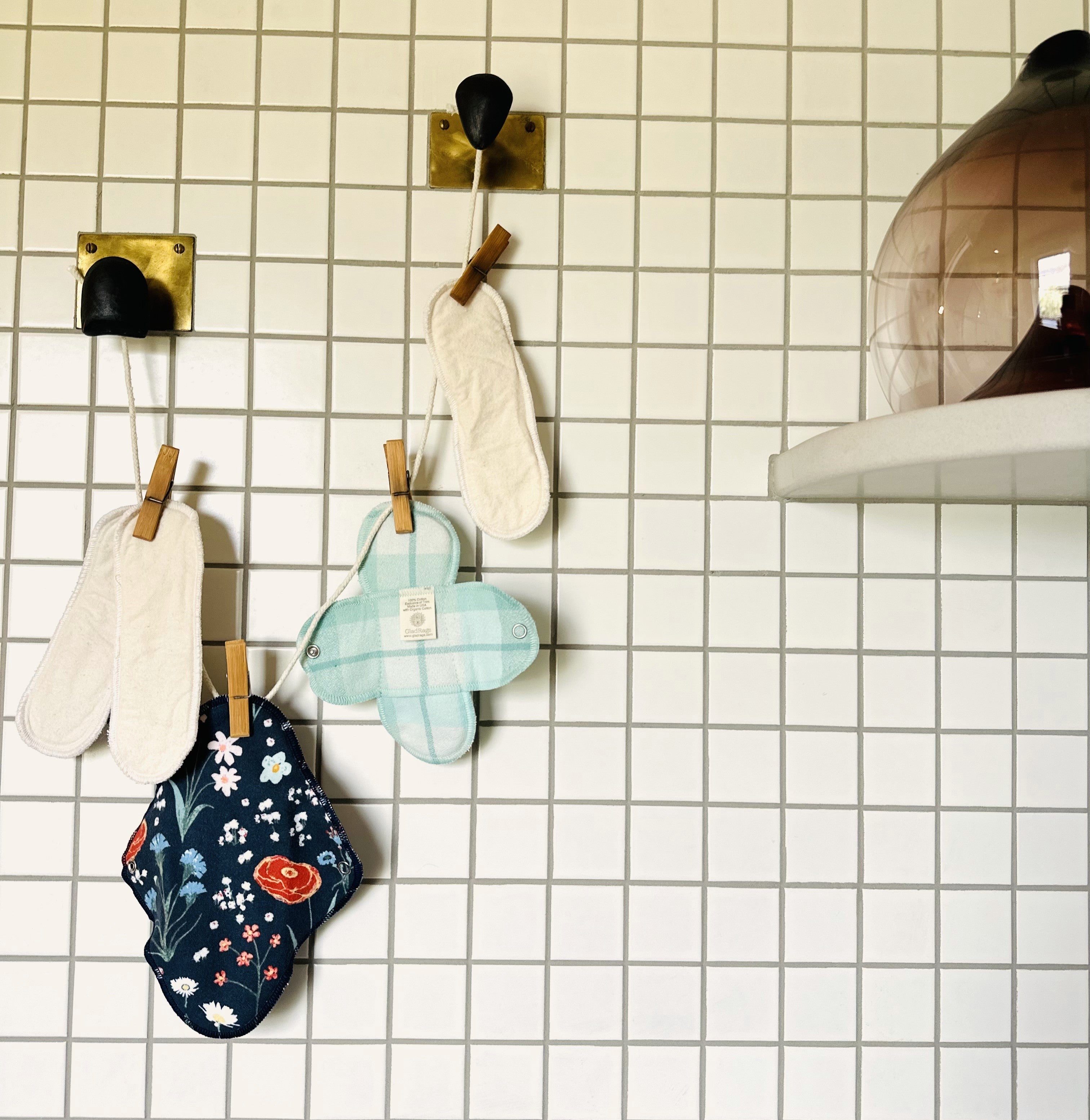 Gladrags reusable pads hang drying in the air pinned on a clothes line in the bathroom